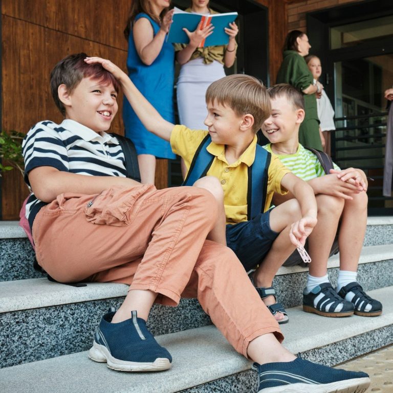 Schulkinder sitzen lachend vor einem Gebäude und spielen zusammen.