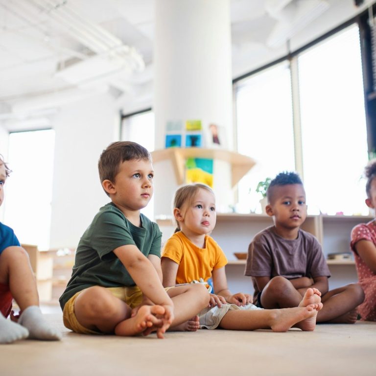 Schulkinder sitzen lachend vor einem Gebäude und spielen zusammen.